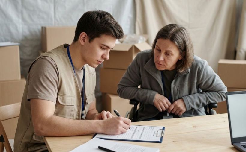 humanitarian worker is helping the person with disability to fill out the forms for MPCA 
